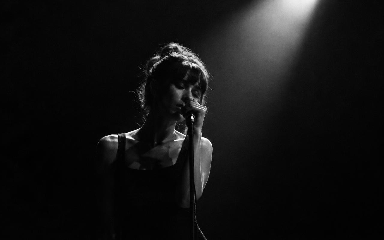 A singer performing under a single hard spotlight on a dark stage